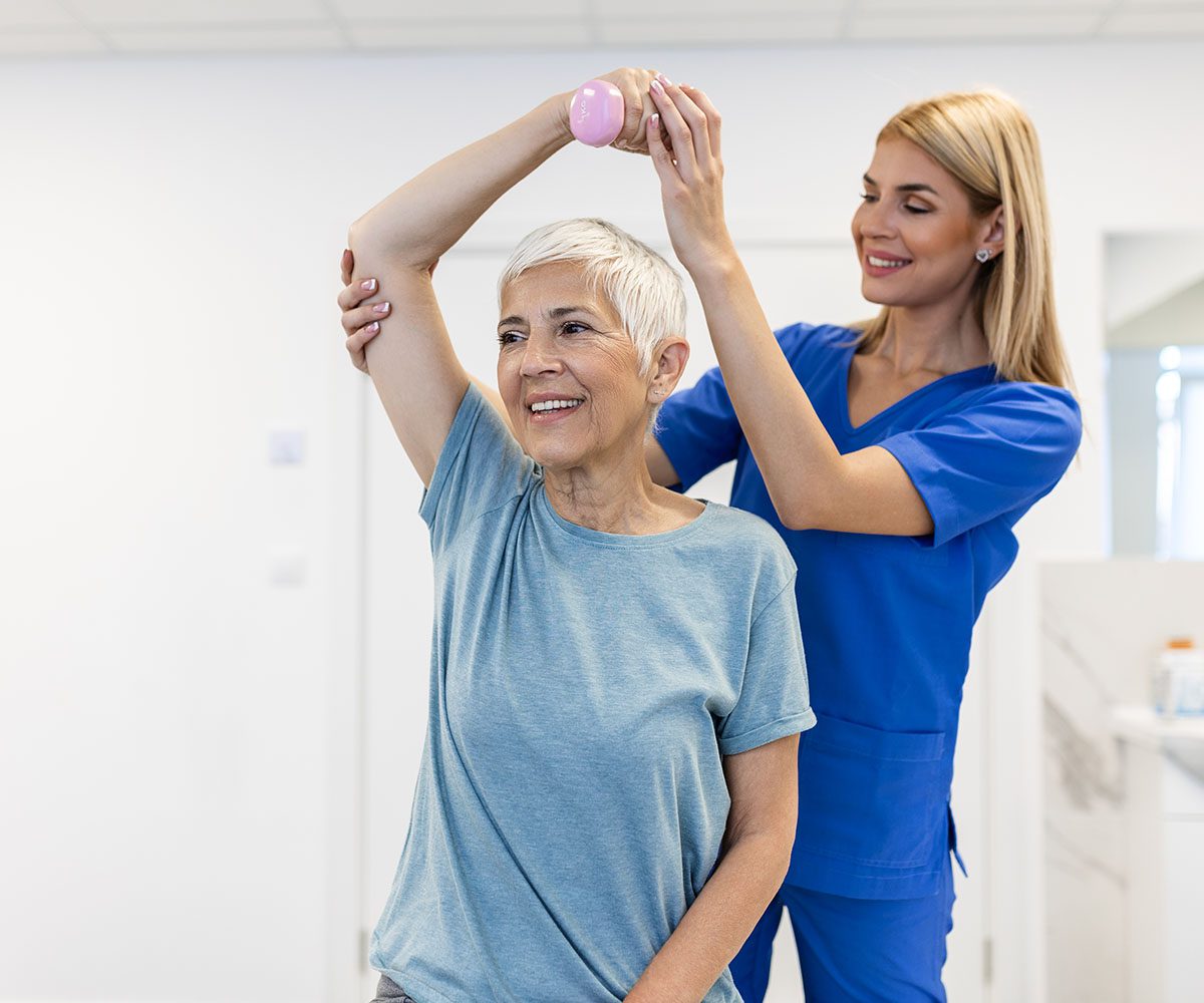 Elderly woman doing arm exercise with assistance.