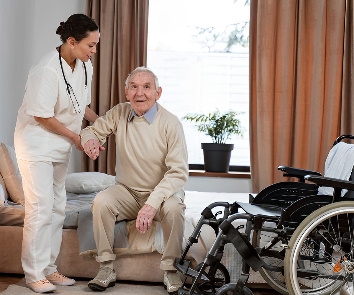 Caregiver assisting elderly man near wheelchair.
