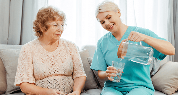 Caregiver pouring water for elderly woman.