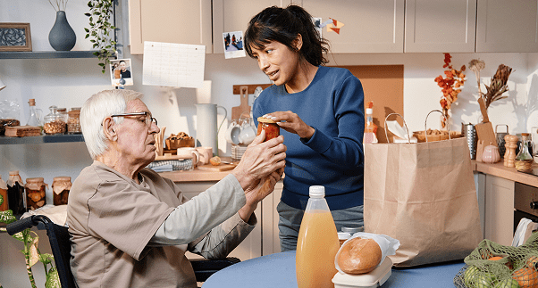 Woman helps elderly man with groceries.