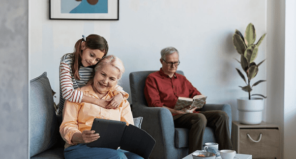 Girl hugging grandmother, man reading on couch.