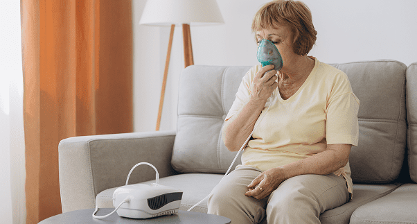 Elderly woman using a nebulizer on sofa.